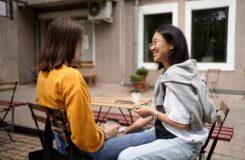 Zwei Frauen unterhalten sich bei Kaffee an einem Café-Tisch im Freien