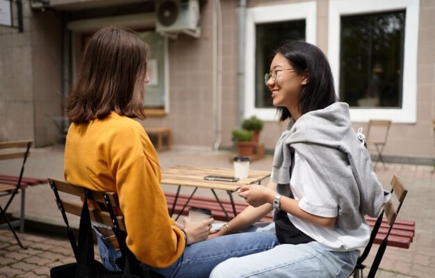 Zwei Frauen unterhalten sich bei Kaffee an einem Café-Tisch im Freien