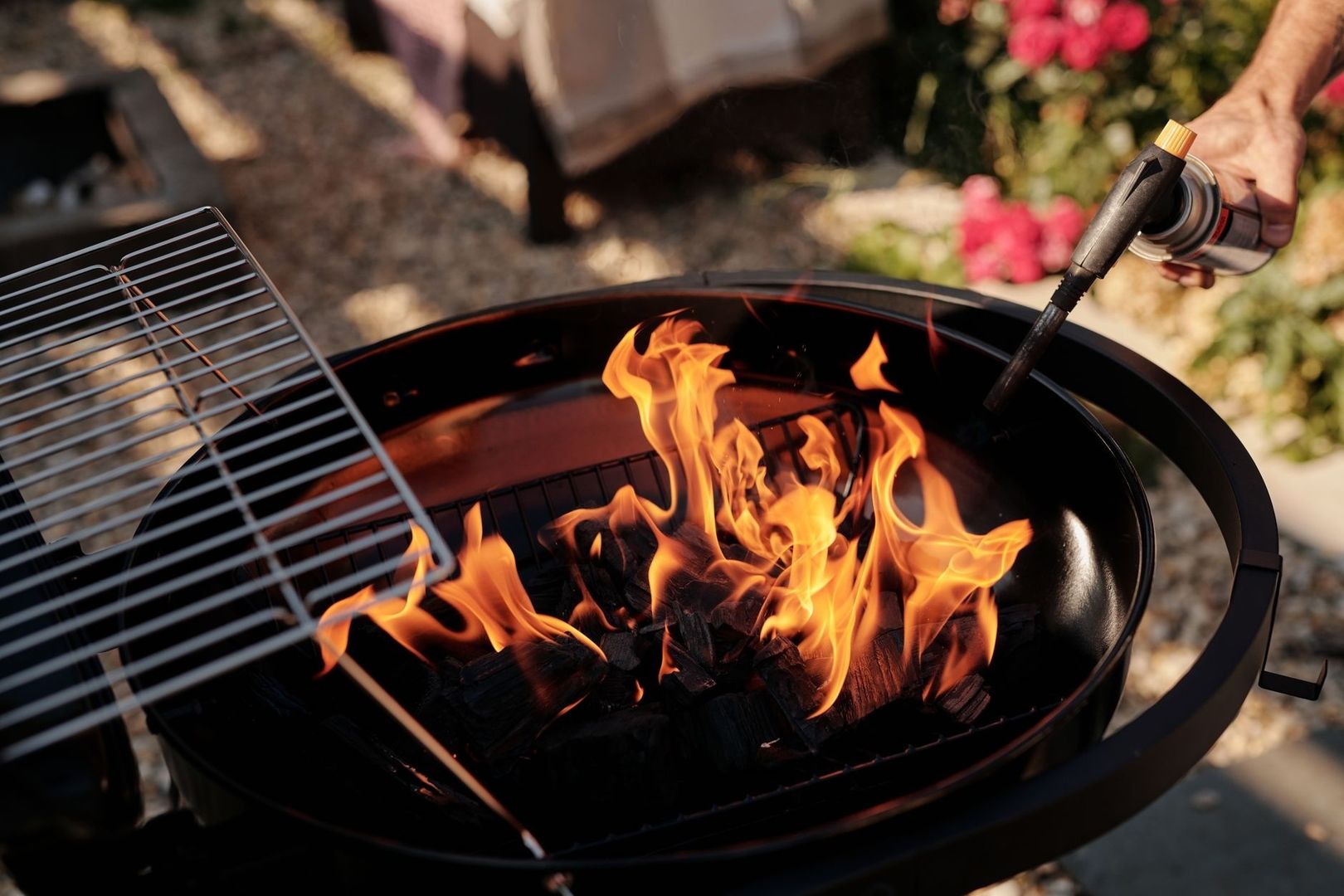 Brennender Holzkohlegrill mit Grillrost und Anzündgerät im Garten